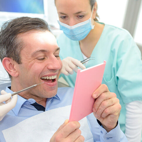man in blue checkered shirt smiling at his reflection in dentist chair