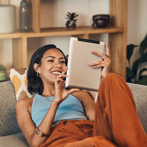 Woman smiling while sitting on couch and watching show on tablet