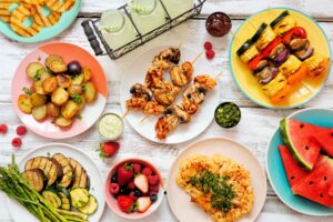 Bird's eye view of a variety of grilled meat, fruits, and veggies on white wooden surface